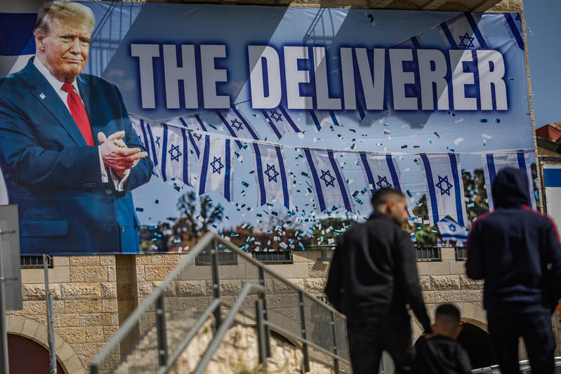 People walk next to a large banner depicting U.S. President Donald Trump with the slogan “The Deliverer” hangs on a building in Jerusalem, April 19, 2026.